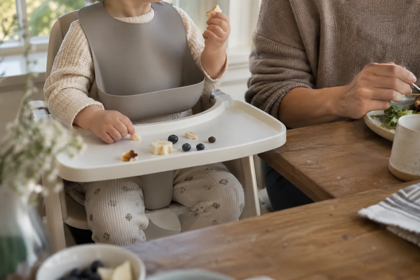 A plain silicone bib hanging above a high-chair tray, with room for its food-catching pocket to stay open in an American dining nook